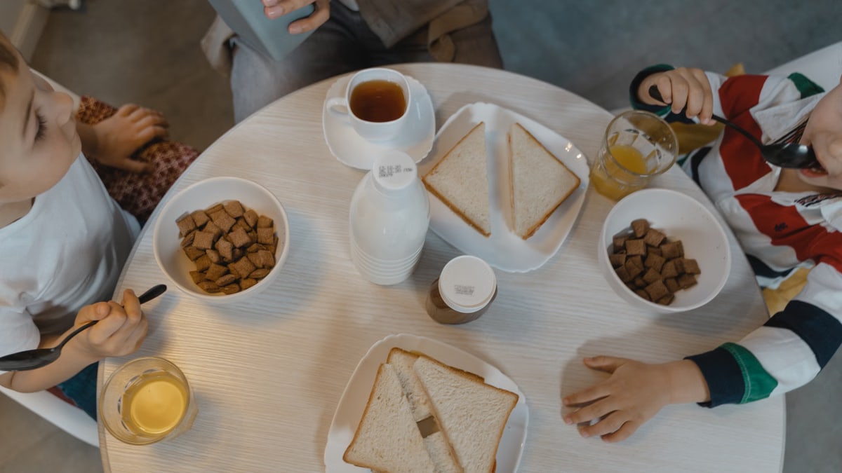 Children enjoying a breakfast with cereal and sliced bread at a cozy indoor dining table.